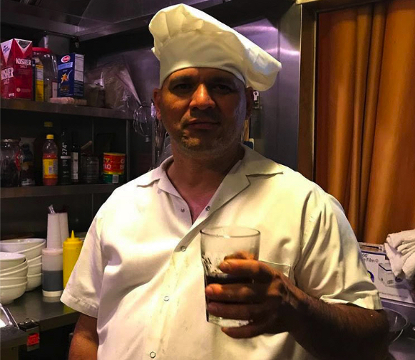 Line Cook Ricardo Flores with a chef hat and a glass of water